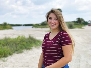 Portrait of smiling young woman standing on beach against sky