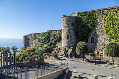 Old building by sea against clear blue sky