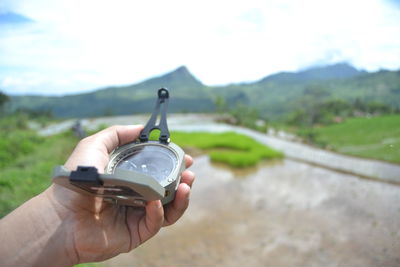 Cropped hand holding navigational compass against sky