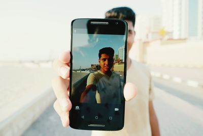 Portrait of young man taking selfie while standing on road against sky