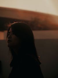 Portrait of young woman looking away against sky during sunset