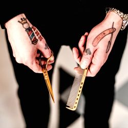 Midsection of barber with tattooed hands holding comb and scissors at shop