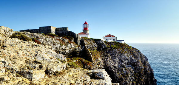 Lighthouse by sea against buildings