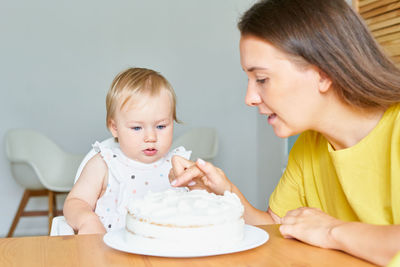 Horizontal of adorable little girl looking at mother tasting creamy birthday cake