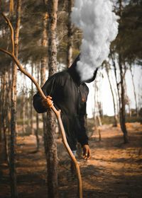 Man standing by tree trunk in forest