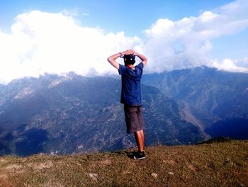 Rear view of man with hands behind head standing by mountains