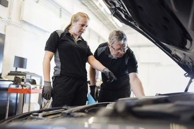 Female mechanic showing car engine to senior man at shop