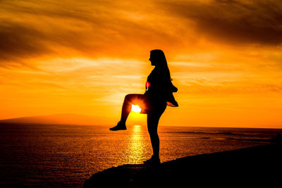 Silhouette woman standing on one leg against sea during sunset