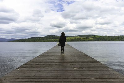 Rear view of woman standing on pier over lake against sky