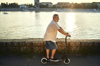 Senior man riding e-scooter at the riverside