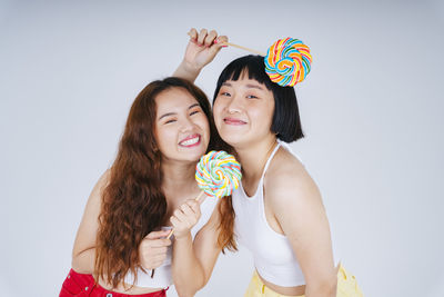 Portrait of lesbian couple holding lollipop against white background