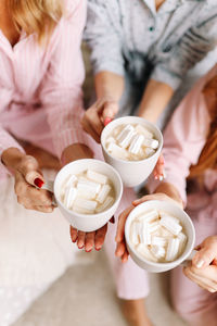 A group of girls in pajamas hold drinks coffee mugs with marshmallows in a cozy room at home