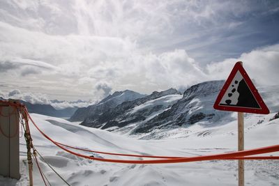 Road sign on snowcapped mountain against sky