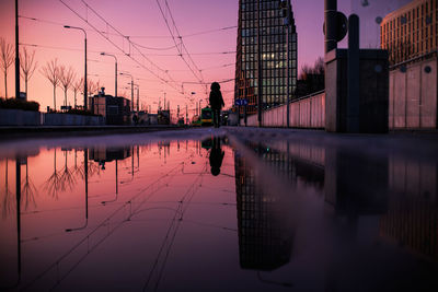 Reflection of person on puddle in city during sunset