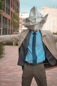 Businessman with newspaper on face standing with arms outstretched in city