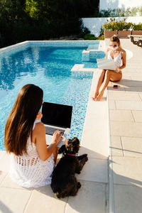 Side view of woman using mobile phone while sitting in swimming pool