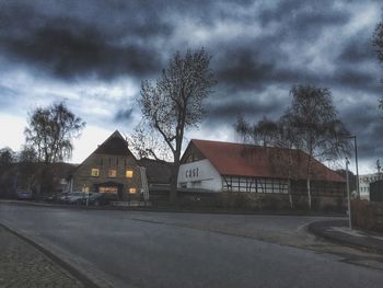 Road leading towards houses against cloudy sky