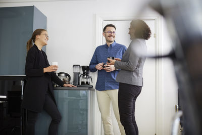 Smiling business colleagues having coffee while talking at office