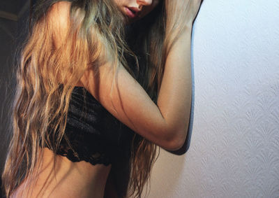 Midsection of young woman with long hair leaning on wall