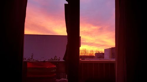 Silhouette buildings against sky during sunset seen through window