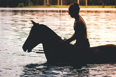 Silhouette of women on horse by lake during sunset