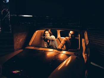 Friends sitting in abandoned illuminated car at night