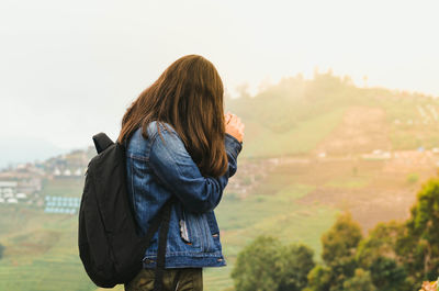 Side view of young woman carrying backpack while standing against landscape