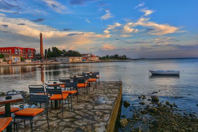 Chairs and tables arranged on pier by sea against sky during sunset