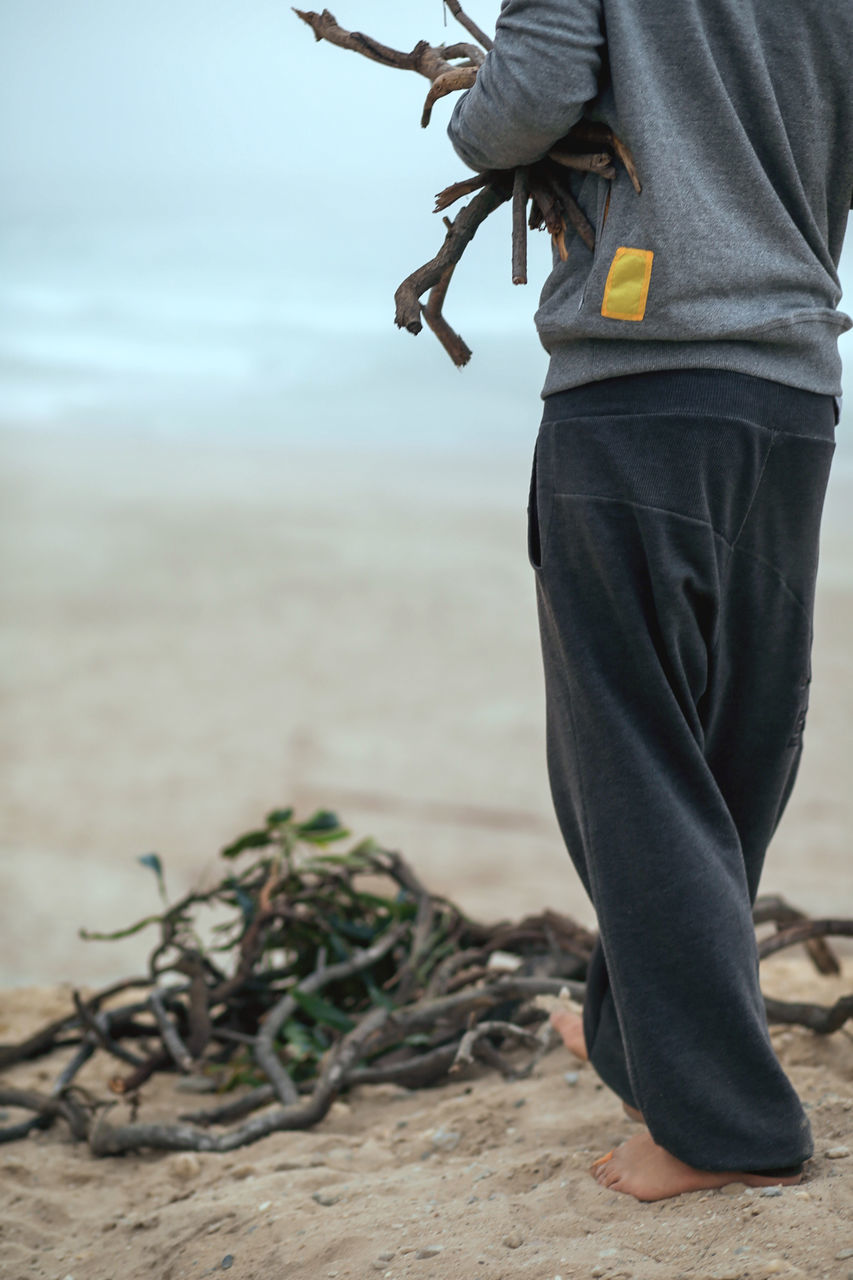 one person, real people, focus on foreground, day, men, nature, land, standing, casual clothing, low section, rear view, lifestyles, beach, outdoors, human leg, leisure activity, holding, water, midsection, jeans