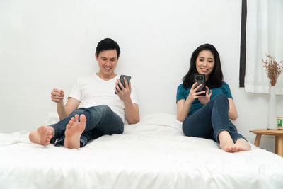 Young woman using phone while sitting on bed