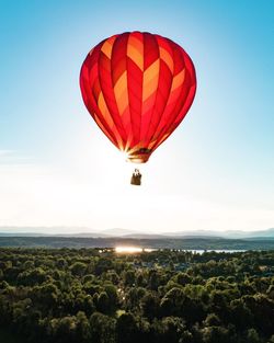 Red hot air balloon flying over landscape against clear sky