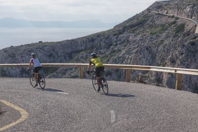 People riding bicycle on road against mountain range