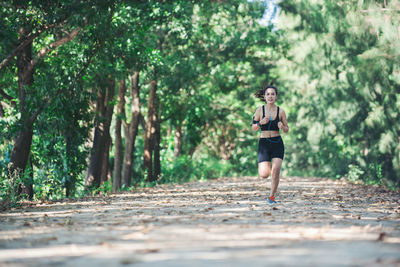 Full length of determined young woman jogging on road amidst trees