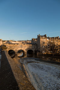 Arch pulteney bridge over river amidst buildings against clear blue sky in bath uk