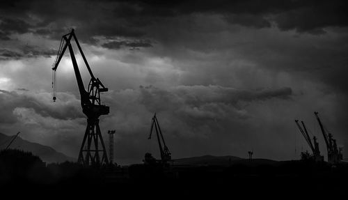 Silhouette cranes on field against sky