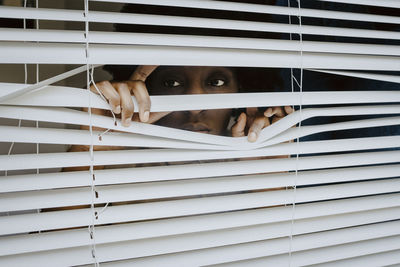 Woman looking away while touching window blinds