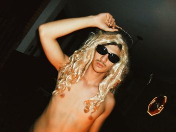 Portrait of shirtless man wearing wig and sunglasses at home