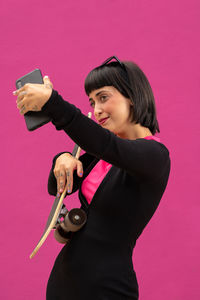 Beautiful woman with short hair posing with a skateboard on a colored background