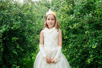 Portrait of girl wearing crown standing against plants