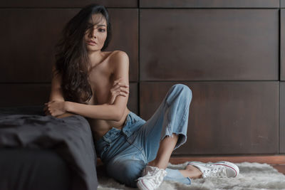 Shirtless young woman sitting on bed