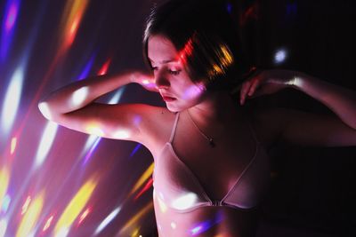 Young woman wearing bikini standing against wall in illuminated room