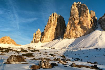 Rock formations by snow covered field against blue sky