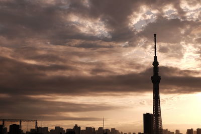 Communications tower in city against cloudy sky