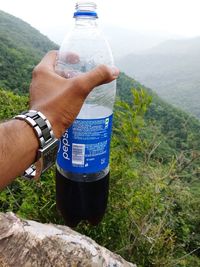 Midsection of man holding glass bottle against mountains