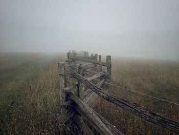 Fence on field against sky in fog