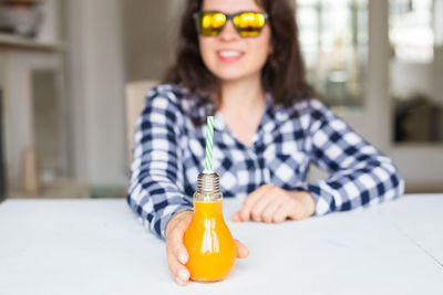 Portrait of young woman holding bottle on table