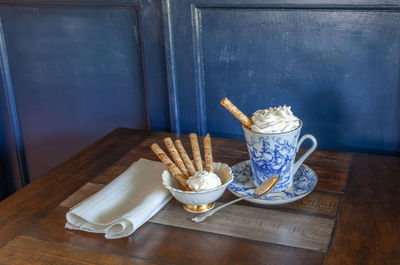 Gourmet hot chocolate and whip cream in a nautical china mug with cookies on a rustic table 