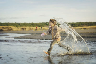 Full length of man splashing water against sky