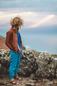 Woman standing by rocks while looking at sea against sky