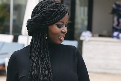 Close-up of smiling mid adult woman with long braided hair standing against building